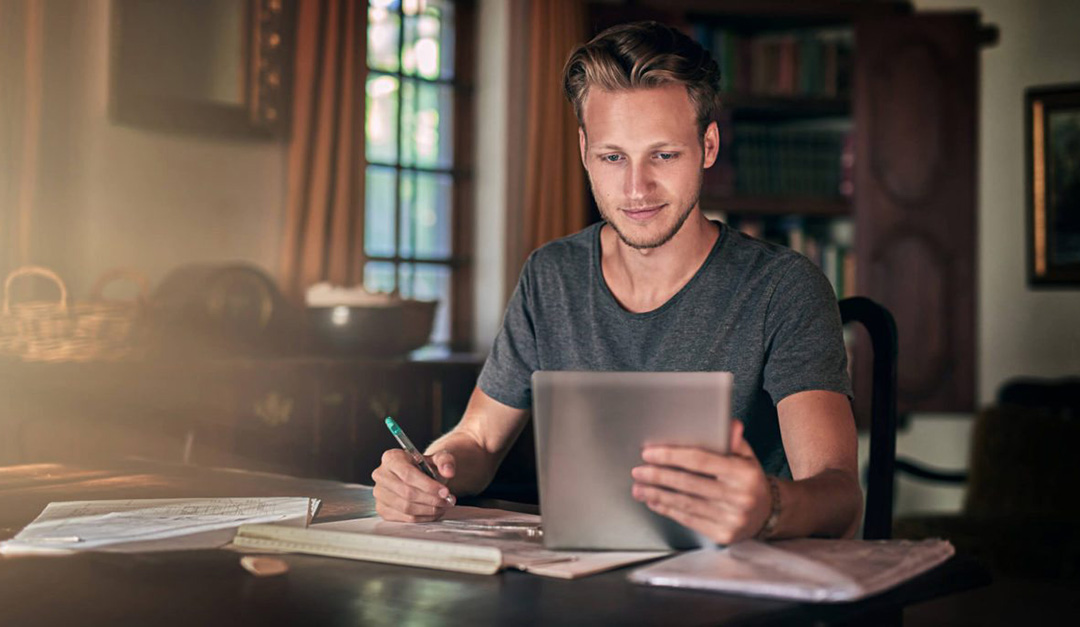 man writing while looking at the ipad