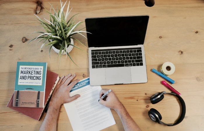 a hand holding a ballpen and Laptop, Books on the table