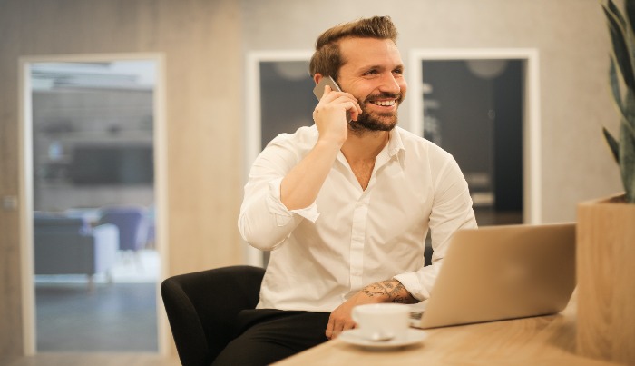 Man talking to the cellphone and has a laptop on the table