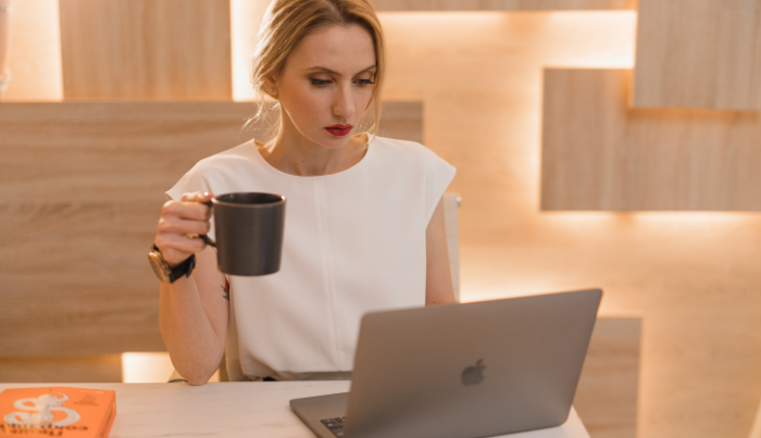Business woman having her coffee while looking at her laptop